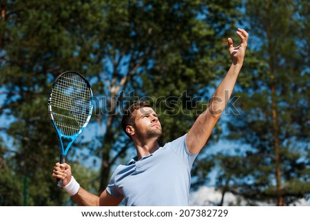 Tennis player serving ball. Low angle view of confident male tennis player serving a ball