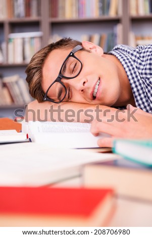 Student sleeping. Handsome young man sleeping while sitting in library and leaning his face at the desk