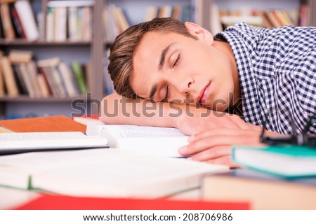 Sleeping in library. Handsome young man sleeping while sitting in library and leaning his face at the desk