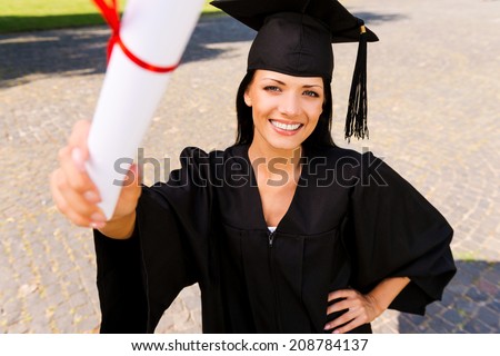 Happy graduate with diploma. Top view of happy young woman in graduation gown showing her diploma and smiling
