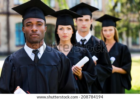 Feeling confident about their future. Four college graduates standing in a row and looking at camera