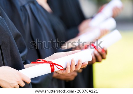 Graduates with diplomas. Close-up of four college graduates standing in a row and holding their diplomas