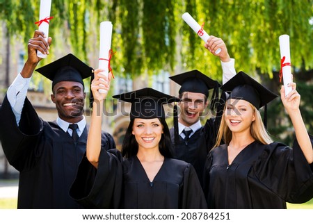 Happy graduates. Four college graduates showing their diplomas and smiling while standing close to each other and