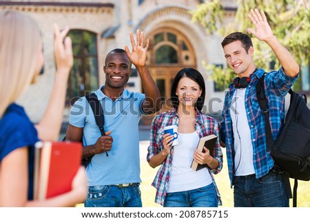 Saying hi to friends. Rear view of young woman holding books and waving to her friends standing outdoors