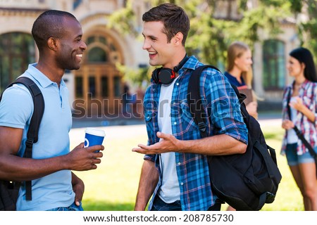 Chatting with friends. Two young men talking to each other and smiling while two women standing in the background