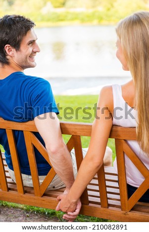 Enjoying their time together. Rear view of beautiful young loving couple sitting on the bench together and holding hands