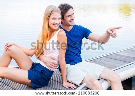 Look at that! Beautiful young loving couple sitting at the quayside together and smiling while man pointing away
