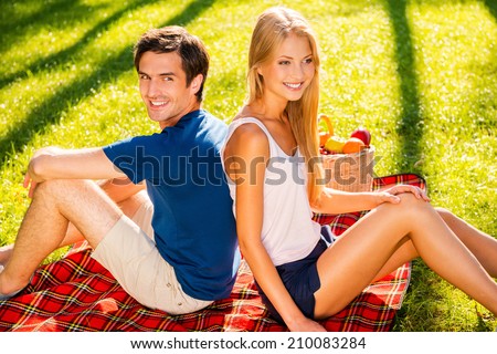 Picnic time. Top view of happy young loving couple having picnic on grass while sitting back to back and smiling
