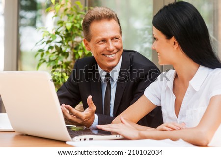 Business talk. Two business people in formalwear discussing something and smiling while both sitting at the table outdoors