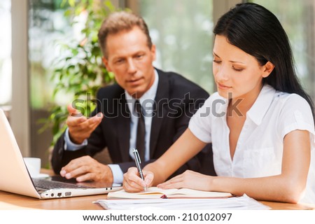 Working on project together. Two business people in formalwear working together while both sitting at the table outdoors