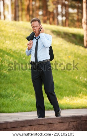 Always staying connected. Serious mature businessman talking on the mobile while walking in park