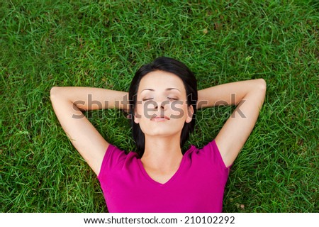 Total relaxation. Top view of beautiful young woman sleeping while holding hands behind head and lying on the green grass