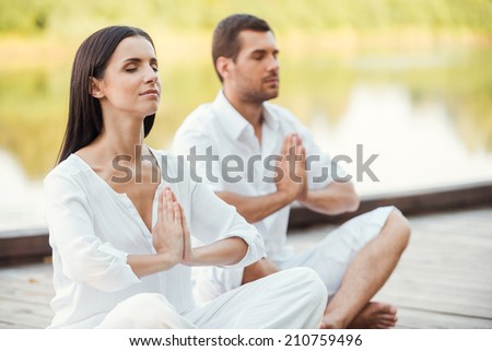 Morning meditation. Beautiful young couple in white clothing meditating outdoors together and keeping eyes closed