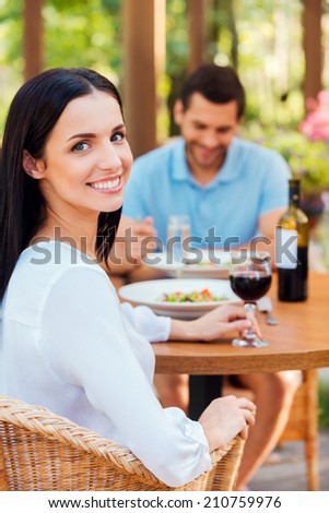 Spending great time in restaurant. Beautiful young couple relaxing in outdoors restaurant together while woman looking at camera and smiling