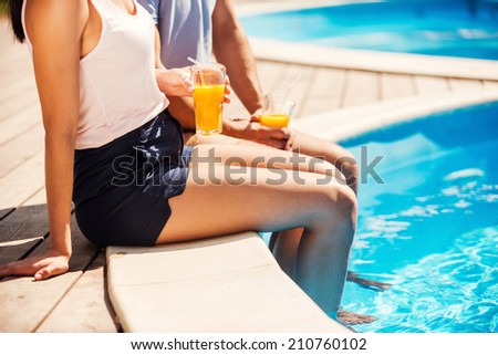 Leisure time poolside. Close-up of couple in casual wear sitting poolside together and drinking cocktails