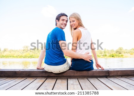 It is our first date. Beautiful young loving couple sitting at the quayside together and looking over shoulder with smile
