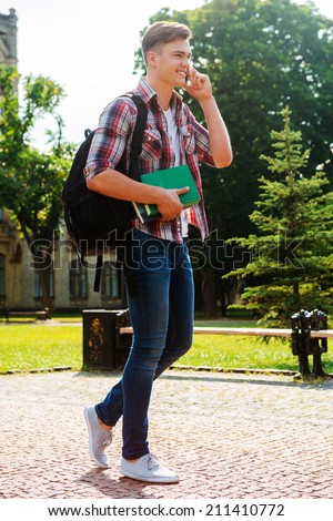 Staying in touch with friends. Full length of handsome male student talking on the mobile phone and smiling while walking outdoors
