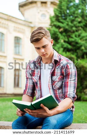 Handsome bookworm. Confident male student reading book while sitting on the bench and in front of university building