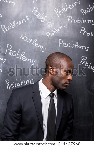 Problems all around me. Depressed African man in formalwear standing against blackboard with inscription Problems