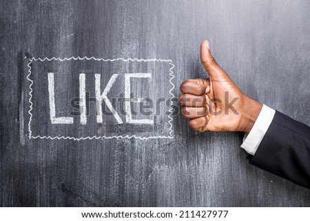 Like this! Close-up of human hand with thumb up in front of the blackboard with inscription Like