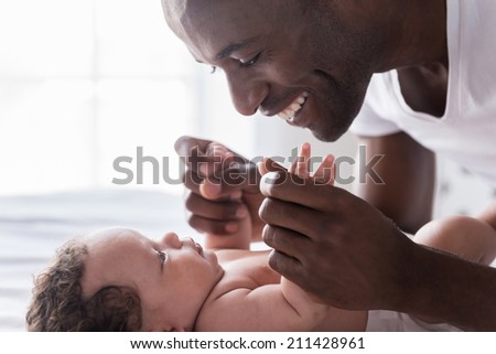 You are my world! Side view of happy young African man playing with his little baby and smiling while lying in bed