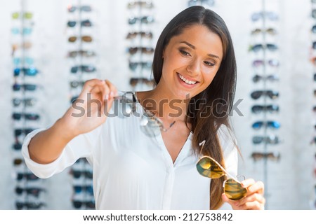 Hard choice. Beautiful young woman choosing sunglasses in store