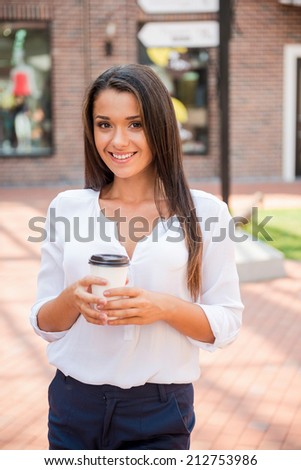 Coffee on the Go. Beautiful young woman holding coffee cup and smiling while standing outdoors