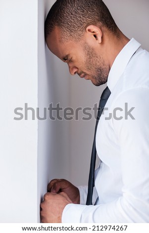 Depressed businessman. Side view of depressed young man in shirt and tie leaning at the wall and keeping eyes closed