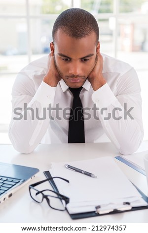 Sick and tired. Depressed young African man in formalwear holding head in hands while sitting at his working place