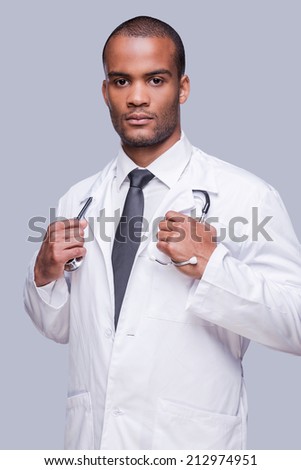 Confident medical expert. Confident African doctor looking at camera and adjusting his stethoscope while standing against grey background