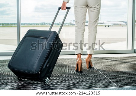 Business trip. Rear view of businesswoman in formalwear carrying suitcase while walking away with airplanes in the background