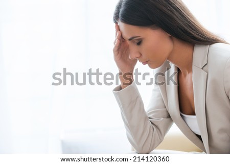 Tired and depressed businesswoman. Side view of depressed young businesswoman in suit touching head with hand and keeping eyes closed while sitting at the chair
