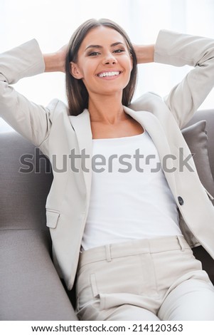 Feeling happy and relaxed. Happy young businesswoman in suit holding hands behind head and smiling while sitting at the chair