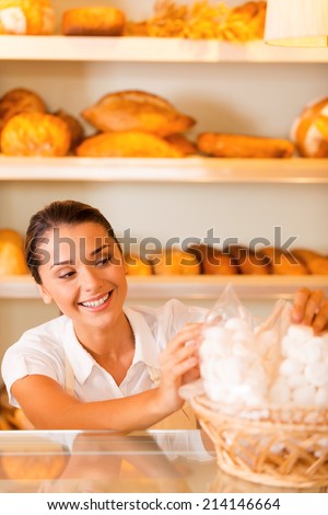 Happy baker at work. Attractive young woman in apron packing cookies and smiling while standing in bakery shop