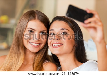 We love making selfie! Two attractive young women making selfie by smart phone