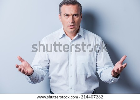 Can you believe it? Frustrated mature man in shirt looking at camera and gesturing while standing against grey background