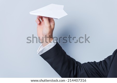 Paper airplane. Close-up of man in formalwear holding paper airplane against grey background