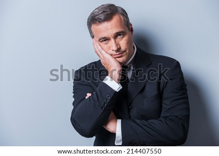 Bored businessman. Bored mature man in formalwear holding head in hand and looking at camera while standing against grey background