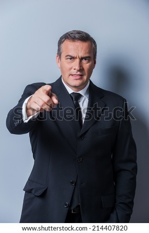 Angry boss. Furious mature man in formalwear pointing you while standing against grey background