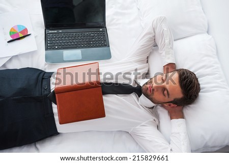 Businessman sleeping. Top view of handsome young man in shirt and tie holding hands behind head and keeping eyes closed while lying in bed at the hotel room
