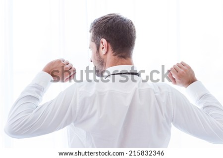 Time to relax. Rear view of man in shirt and tie standing against window and raising his arms
