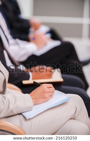 People making notes. Close-up side view of business people writing something in their note pads while sitting in a row