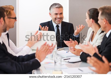 Successful business team. Confident mature man in formalwear smiling and gesturing while his colleagues applauding to him