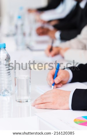 Business people at work. Close-up of business people writing something in their note pads while sitting in a row