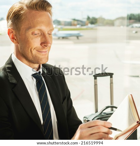 Businessman making notes. Side view of confident businessman in formalwear writing something in note pad while waiting for a flight in airport