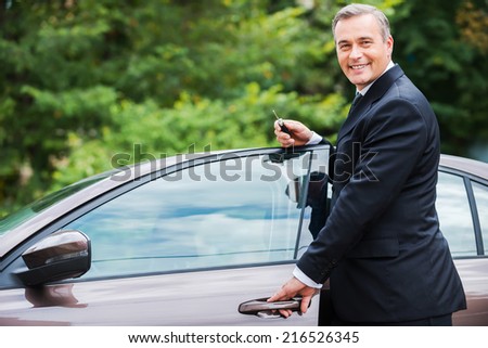 This car is perfect for me. Cheerful mature man in formalwear looking at camera and smiling while standing near his new car