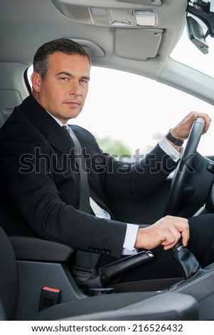 Businessman in car. Side view of confident mature businessman driving car and looking at you