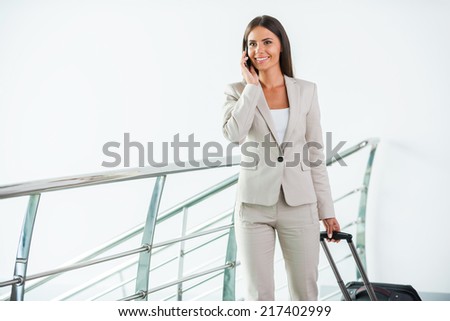 Businesswoman on the go. Beautiful young businesswoman in suit talking on the mobile phone and smiling while getting out of elevator