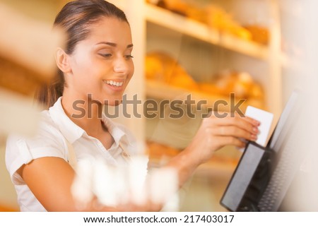 Cashier at work. Attractive young female cashier swipes a plastic card through a machine and smiling