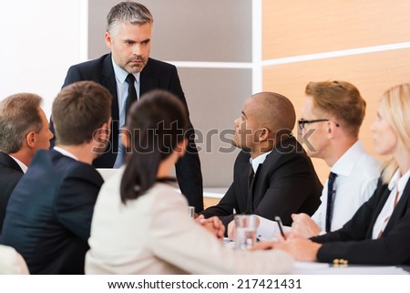 Urgent business meeting. Business people in formalwear sitting at the table together while their boss standing and looking at them